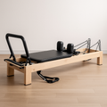 Angled view of Pulserig Pilates reformer, showing carriage, ropes, and adjustable headrest for home workouts